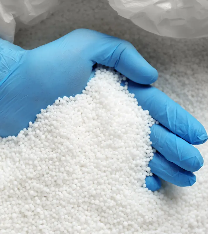 Mano con guanto blu che solleva i granuli bianchi di materiale termoindurente